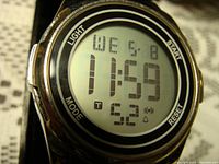 Close-up photo of the watch face displaying the digital time, day, date, and alarm icons with bezel buttons labeled Light, Mode, Start, Reset.