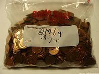 Clear resealable plastic bag filled with a large quantity of US pennies, showing copper color and some signs of circulation wear. Label on bag indicates weight as 2146 grams and price as $7+.
