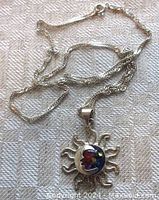 Full view of the sterling silver sun and man in the moon pendant with attached sterling chain laid flat on a textured fabric surface.