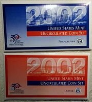 Two coin set envelopes from 2002 United States Mint, one blue Philadelphia and one red Denver, each labeled as Uncirculated Coin Set.