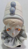 Front view of porcelain clown bust showing detailed face and hat with two pom-poms.