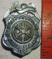 Front view of vintage East Andover Fire Dept No. 12 silver tone badge on a fabric background with a measuring tape to the side for scale.