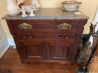 Front view of antique wooden chest showing marble top, two drawers with ornate brass handles and lower cabinet doors.