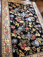 Full view of the large rectangular floral hooked rug with black field and floral borders.