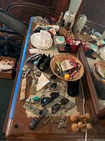 Wide view of wooden dresser top showing scattered sunglasses, keys, belt buckles, perfume bottles, trinket boxes, and wooden bowling pins near mirror.