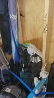 Photo showing multiple folding chairs and umbrellas stored upright in a wooden shed, bound by a blue strap.