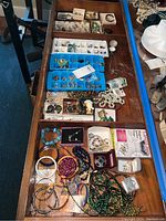 Photo of assorted costume jewelry items laid out including earrings, necklaces, bracelets, and pins in an open drawer