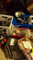 Overview photo showing crates with various items like wires, Black and Decker branded box, pens, pencils, and candles showing lot contents.