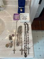 Overall view of lot showing ring box, egg pendant box, crucifix box, medal charms and rosaries on countertop