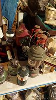 Photo shows green Coleman lantern, two red metal lanterns, a metal flashlight, and boxes of replacement globes on a table in a basement setting.