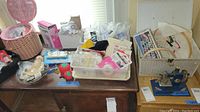 Wide shot of sewing supplies including boxes, baskets and pin cushions on a wooden table