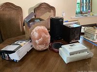 Lot of two space heaters, Himalayan salt lamp, CarMD vehicle health system box, Aprilaire thermostat, and personal mirror on wooden table.