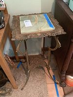 Full view of metal stand with square marble top, sitting on carpeted floor, with rust and wear visible.