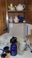 Full view of cabinet and counter with assorted tea pots, bowls, crock, and jars