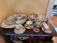 Photo showing various teacups, saucers, creamers, small bowls and a large floral serving platter on a wooden surface.