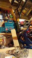 Wide-angle photo showing multiple hand tools, socket set in blue case, blue power drill, boxes with hardware and tools scattered on concrete floor.
