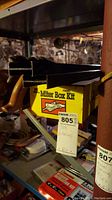 Shelf featuring a yellow miter box kit with black saws and miscellaneous tools beneath on shelves in basement.