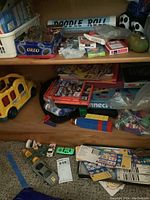 Wooden shelf with assorted toys including flash cards, playing cards, crayons, markers, toy vehicles, and building blocks scattered on shelves and floor.