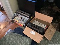 View of assorted VHS tapes next to electronic devices including two players