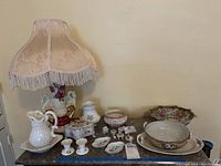 Full view of the lamp with fringed shade alongside various ceramic pieces placed on a marble surface.