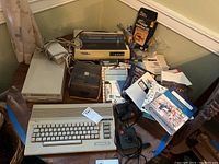 Overview of lot showing Commodore 64 keyboard, Commodore 1541 disk drive, joysticks, floppy disks, software manuals, power supply and Seikosha printer.