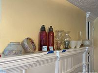Overview showing multiple vintage glass and sterling lamp shades and various decorative glass pieces arranged on a mantle.