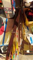 Top view showing the recurve bow, multiple wooden practice arrows with colorful fletchings, a triangular wooden target box, and a wooden cane.