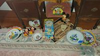Wide view showing all collectible items including Disney plates, Mickey and Minnie figures, Snoopy suitcase and heat pinball game.