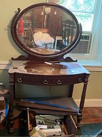 Front view of vintage wood vanity with oval mirror and two drawers, showing adhesive residue on surface and some wear.