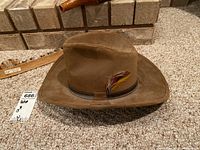 Front view of medium size brown suede cowboy hat with decorative feather on the leather band.