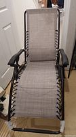 Front view of folding patio chair showing light gray mesh fabric, black frame, armrests, and attached lumbar pillow.