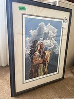 Framed Native American print with cloudy sky, held by a figure wearing traditional feathered headdress and holding a bison skull, including frame and size label.