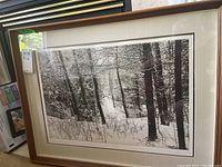 Front view of framed black and white print showing snowy forest with trees and snow on ground, framed in wood with beige mat