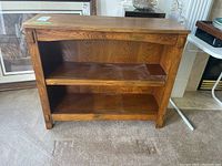 Full front view of wooden shelving unit with two shelves on a carpeted floor near framed artwork.