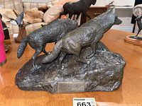 Front view of the metal statue showing the two wolves standing on a rocky base with the signature plaque visible.