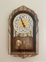 Front view of slag glass wall clock showing clock face and pendulum with stained glass frame.