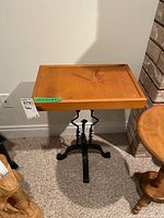 Overall view of the table showing wood top and metal frame against a wall, carpeted floor, and adjacent wooden furniture.