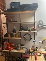 Wide shot of shelves with assorted power tools and hand tools including sanders, planer, clamps, spray bottle, charger, and measuring tapes.