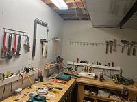 Wide view of workbench with various tools on the wall above it including wrenches, hammers, levels, and clamps