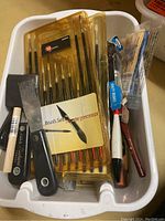 Paintbrushes, paint scrapers, and various small painting tools in a white plastic container.