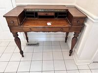 Full front view of antique wood secretary desk showing fold-down writing surface open, multiple compartment pigeonholes, two side drawers, main drawer below, turned carved legs.