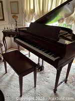 Three-quarter view of baby grand piano with lid open and matching bench in front on patterned rug
