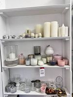 Wide view of candles and holders on white shelving in various colors, shapes, and sizes.