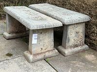 Two identical concrete garden benches side by side, angled view showing top and side detailing