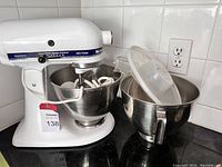 Mixer on base with one bowl attached containing power cord and attachments, extra bowl beside unit
