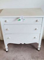 Front view of white dresser showing three drawer fronts and turned legs with casters