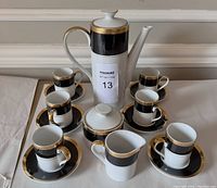 Full set arranged showing coffee pot, cups and saucers, creamer and sugar bowl, all in black, white and gold Mikasa Art Deco style.