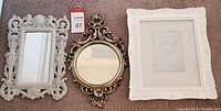 Three wall decor pieces on carpet: white ornate rectangular mirror, round gold mirror, white decorative frame