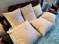 Two standard size and four 18-inch square accent pillows with cream-colored fabric covers arranged on a bed, showing overall set and condition.