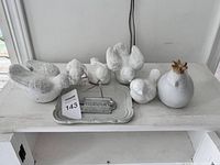 Front-facing photo showing six white clay bird figurines, off-white tray, and metal Farm sign on a white surface.